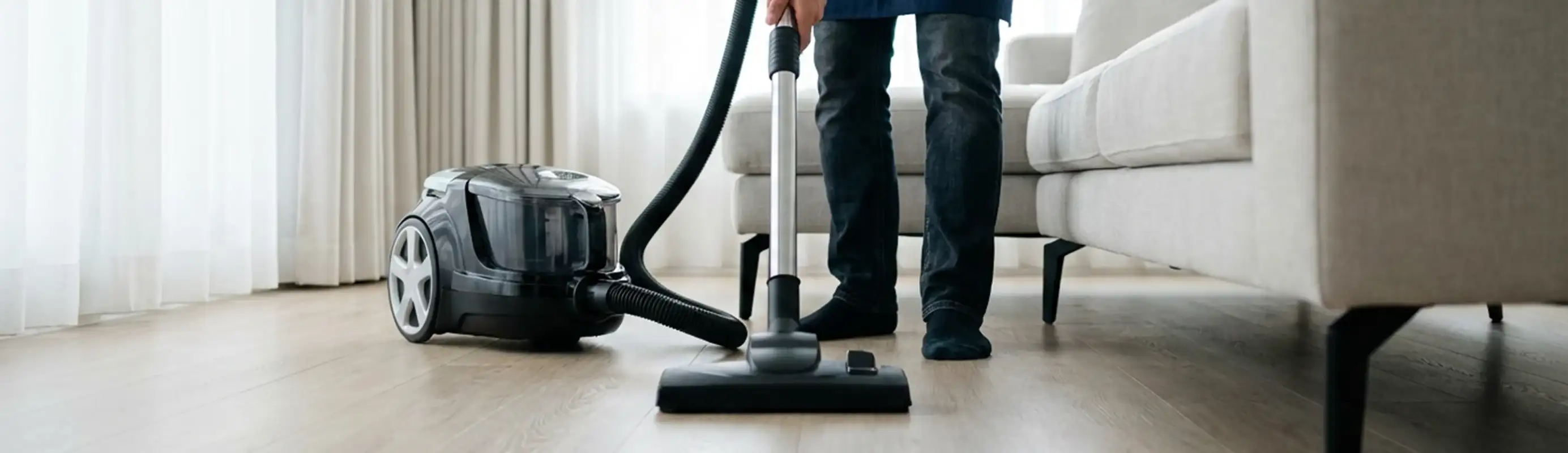 Professional house cleaner vacuuming a living room floor with a canister vacuum cleaner, Bellevue, WA.