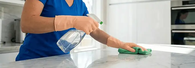 Maid service worker spraying and wiping a kitchen countertop with a microfiber cloth for sanitizing, Bellevue, WA.