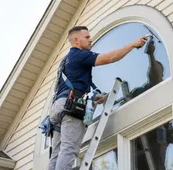 Professional window cleaner on a ladder using a squeegee to clean an exterior arched window, Bellevue, WA.