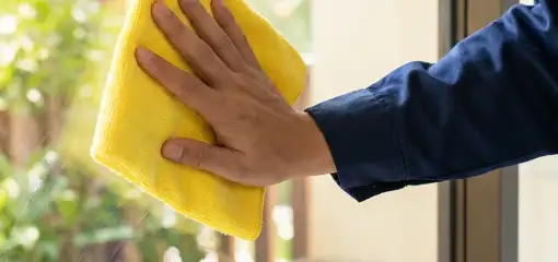 House cleaner wiping a glass window with a yellow microfiber cloth for streak-free cleaning, Bellevue, WA.